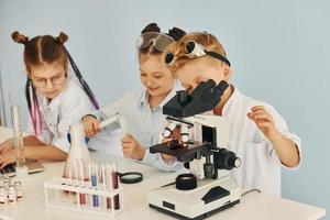 Using microscope. Children in white coats plays a scientists in lab by using equipment photo