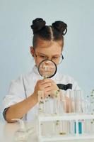 Workes with liquid that is in test tubes. Little girl in coat playing a scientist in lab by using equipment photo