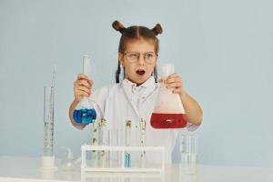 Scared little girl in coat playing a scientist in lab by using equipment photo