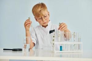 Uses test tubes. Little boy in coat playing a scientist in lab by using equipment photo