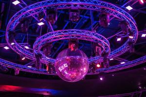 night disco club with neon blue violet red light, disco mirror ball and bright floodlight with round metal frame luminous construction photo