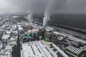 vista aérea panorámica invernal del humo oscuro de las tuberías de la empresa de carpintería con nieve. concepto de contaminación del aire y el agua. foto