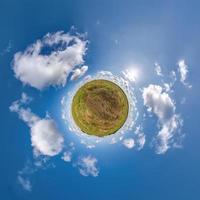 green tiny planet in blue sky with beautiful clouds with transformation of spherical panorama 360 degrees. Curvature of space. photo