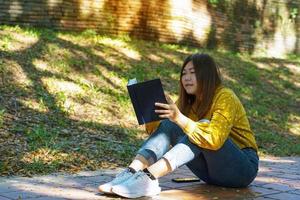 Asian woman sitting with her legs crossed on the floor reading a book Female concept doing outdoor activities such as reading, working, listening to music, having a picnic, etc. photo