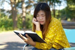 mujer asiática leyendo un libro en una silla de jardín en el parque. concepto haciendo actividades al aire libre como leer, trabajar, escuchar música, hacer un picnic, etc. enfoque suave y selectivo. foto