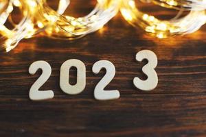 wooden number 2023 on christmas shiny wooden background. with sparkle festive gold garland photo