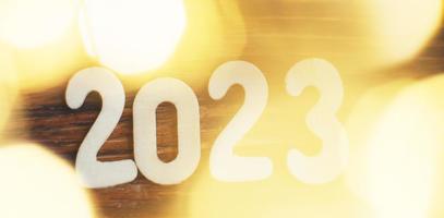 wooden number 2023 on christmas beautifull shiny gold background. sparkle festive blurred bokeh photo