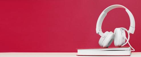 Audio book concept with headphones and a book on a viva magenta background. Listening to a book. photo