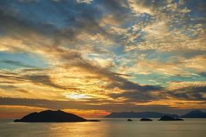 Beautiful sunset sky with clouds over the sea, sunlight glare on the water. Silhouettes of a range of islands on horizon. Idea for background or wallpaper. Breathtaking dramatic sunset, vacation time photo