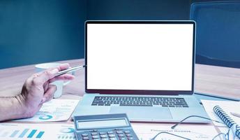 Businessman hand holding a pen to mock up sales summary slide show presentation on display laptop with calculator ,glasses and paper work on table in meeting room photo