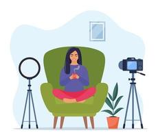 Blogger communicates in live stream with followers. Woman records video sitting in armchair in a Lotus pose and holds a mug of hot drink in her hands. Influencer creating video. Vector illustration.