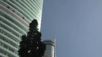 tiro de steadicam de ángulo bajo de primer plano del edificio de oficinas de fachada de vidrio moderno en el distrito de negocios con espejo de pared de vidrios con cielo azul video