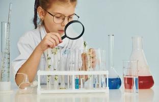 Workes with liquid that is in test tubes. Little girl in coat playing a scientist in lab by using equipment photo