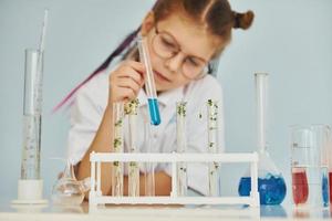 Workes with liquid that is in test tubes. Little girl in coat playing a scientist in lab by using equipment photo