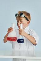 Little boy in coat playing a scientist in lab by using equipment photo