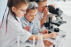 vista lateral. los niños con batas blancas juegan a los científicos en el laboratorio usando equipos foto