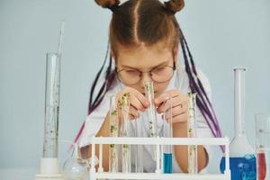 Workes with liquid that is in test tubes. Little girl in coat playing a scientist in lab by using equipment photo