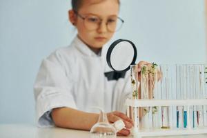 Holds magnifying glass. Little girl in coat playing a scientist in lab by using equipment photo