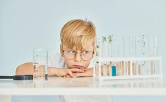 Uses test tubes. Little boy in coat playing a scientist in lab by using equipment photo