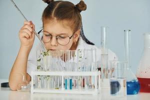 Workes with liquid that is in test tubes. Little girl in coat playing a scientist in lab by using equipment photo
