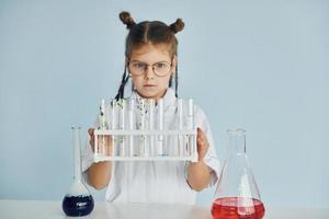 Works with test tubes. Little girl in coat playing a scientist in lab by using equipment photo