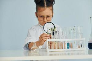 Holds magnifying glass. Little girl in coat playing a scientist in lab by using equipment photo