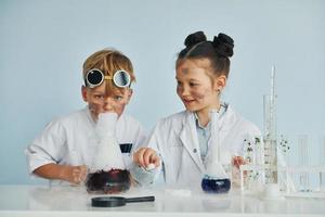 chico trabaja con líquido en tubos de ensayo. los niños con batas blancas juegan a los científicos en el laboratorio usando equipos foto