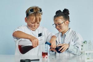 una niña y un niño con batas blancas juegan a los científicos en el laboratorio usando equipo foto