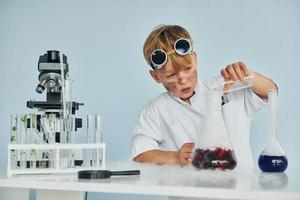 niño pequeño con abrigo jugando a un científico en el laboratorio usando equipo foto