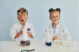 Girl with boy working together. Children in white coats plays a scientists in lab by using equipment photo