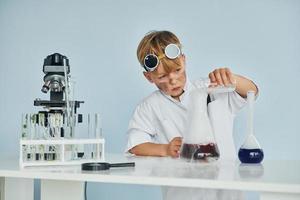 Little boy in coat playing a scientist in lab by using equipment photo