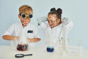 chica con chico trabajando juntos. los niños con batas blancas juegan a los científicos en el laboratorio usando equipos foto