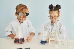 chica con chico trabajando juntos. los niños con batas blancas juegan a los científicos en el laboratorio usando equipos foto