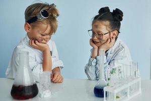 chica con chico trabajando juntos. los niños con batas blancas juegan a los científicos en el laboratorio usando equipos foto