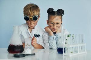 chica con chico trabajando juntos. los niños con batas blancas juegan a los científicos en el laboratorio usando equipos foto