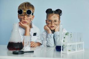 chica con chico trabajando juntos. los niños con batas blancas juegan a los científicos en el laboratorio usando equipos foto