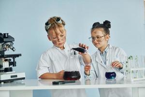 Little girl and boy in white coats plays a scientists in lab by using equipment photo