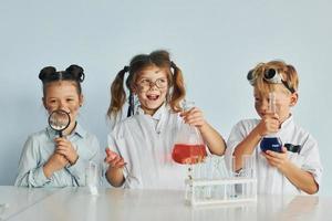 Happy friends smiling. Children in white coats plays a scientists in lab by using equipment photo