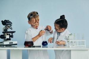 una niña y un niño con batas blancas juegan a los científicos en el laboratorio usando equipo foto