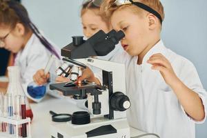 utilizando microscopio. los niños con batas blancas juegan a los científicos en el laboratorio usando equipos foto