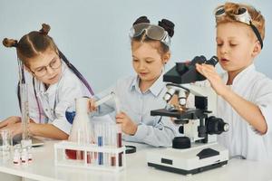 Using microscope. Children in white coats plays a scientists in lab by using equipment photo