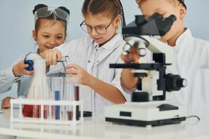 Using microscope. Children in white coats plays a scientists in lab by using equipment photo