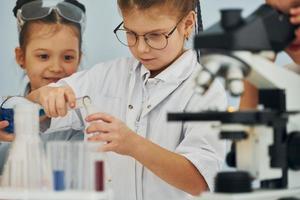 Using microscope. Children in white coats plays a scientists in lab by using equipment photo