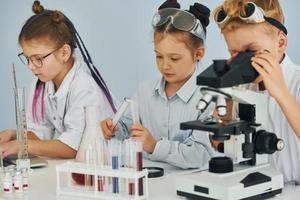 Using microscope. Children in white coats plays a scientists in lab by using equipment photo