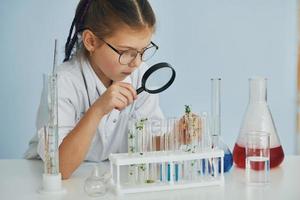Works with test tubes. Little girl in coat playing a scientist in lab by using equipment photo