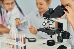 Using microscope. Children in white coats plays a scientists in lab by using equipment photo