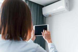 Controlling conditioner by tablet. Young woman is indoors in room of modern house at daytime photo