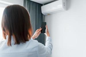 Controlling conditioner by tablet. Young woman is indoors in room of modern house at daytime photo