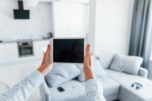 Digital tablet in hands. Young woman is indoors in smart house room at daytime photo