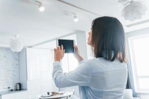 Digital tablet in hands. Young woman is indoors in smart house room at daytime photo